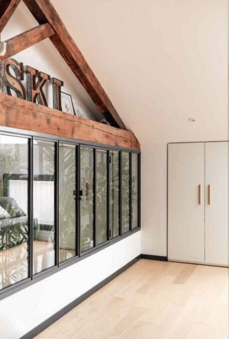 Intérieur de maison avec poutres apparentes, verrière et plantes vertes