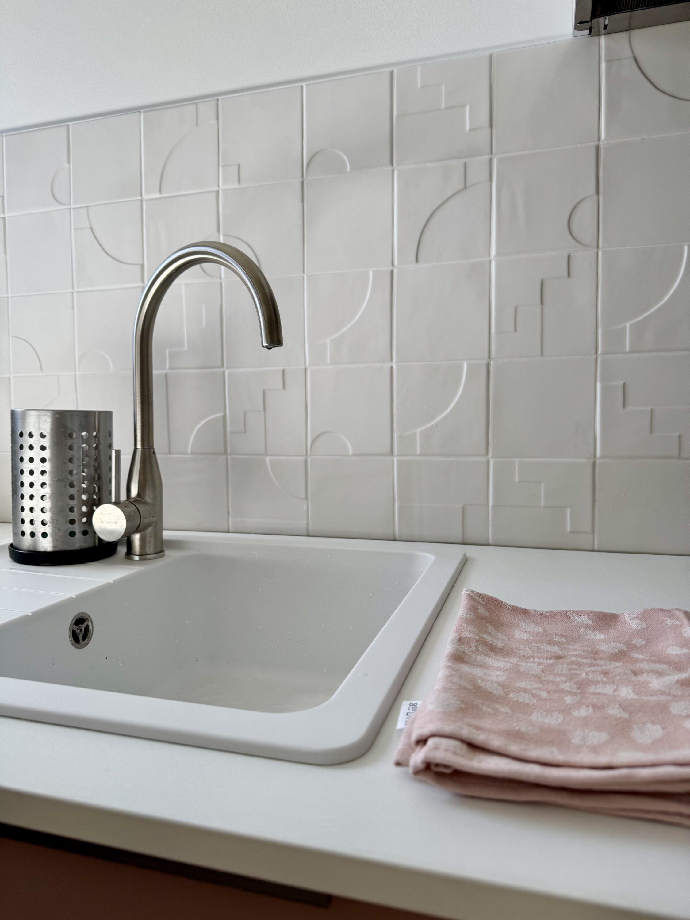 Salle de bain moderne avec robinet argenté, évier blanc, et serviette rose.