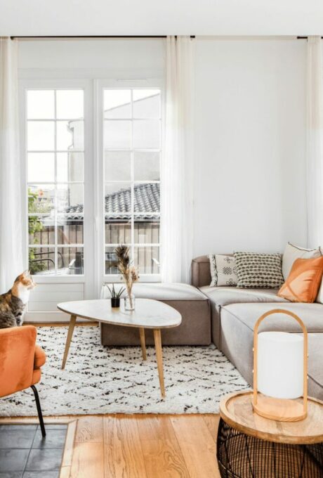 Salon cosy avec grandes fenêtres, canapé d'angle et accents orange