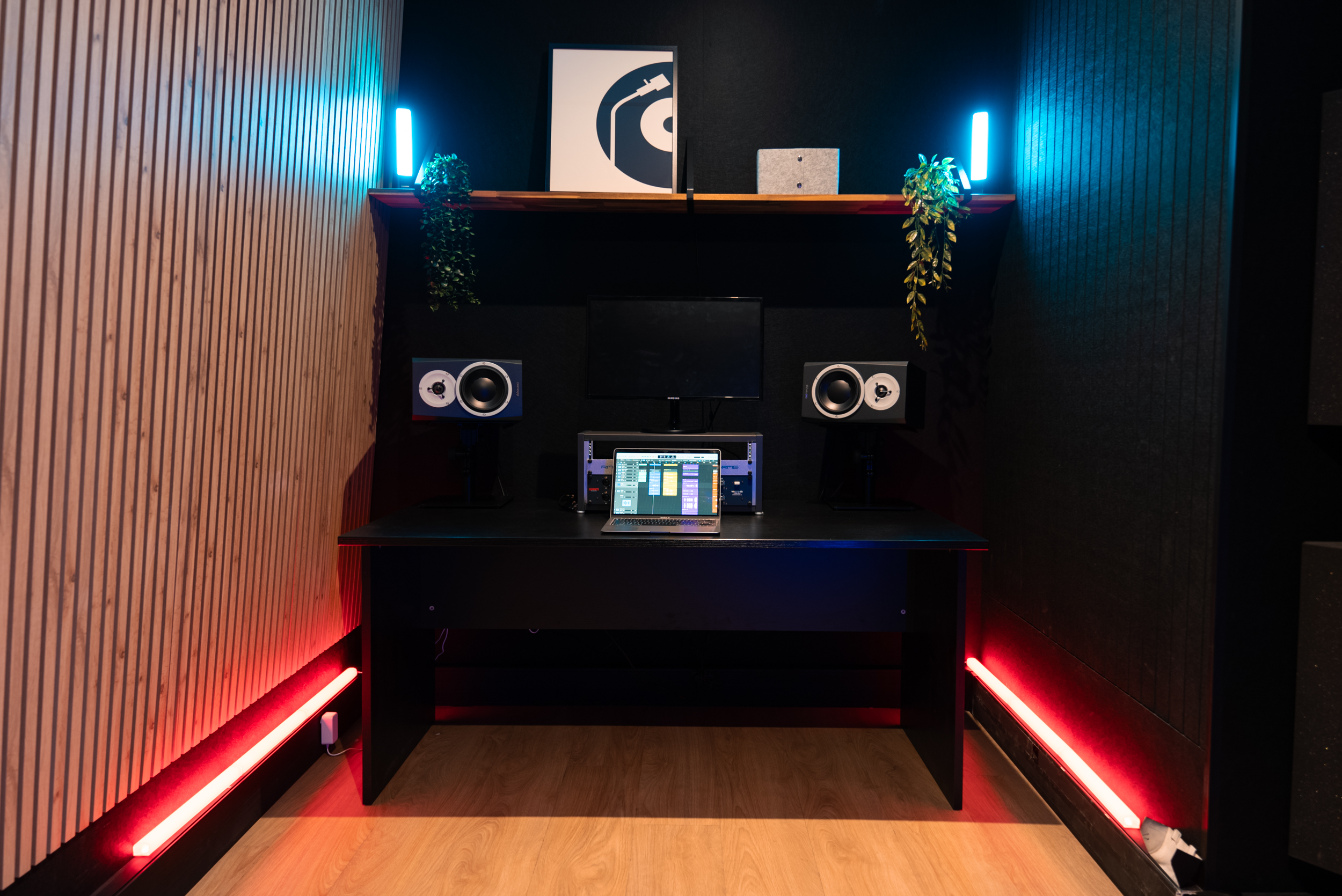 Bureau moderne avec éclairage LED, ordinateur, enceintes, plantes, décoration murale.