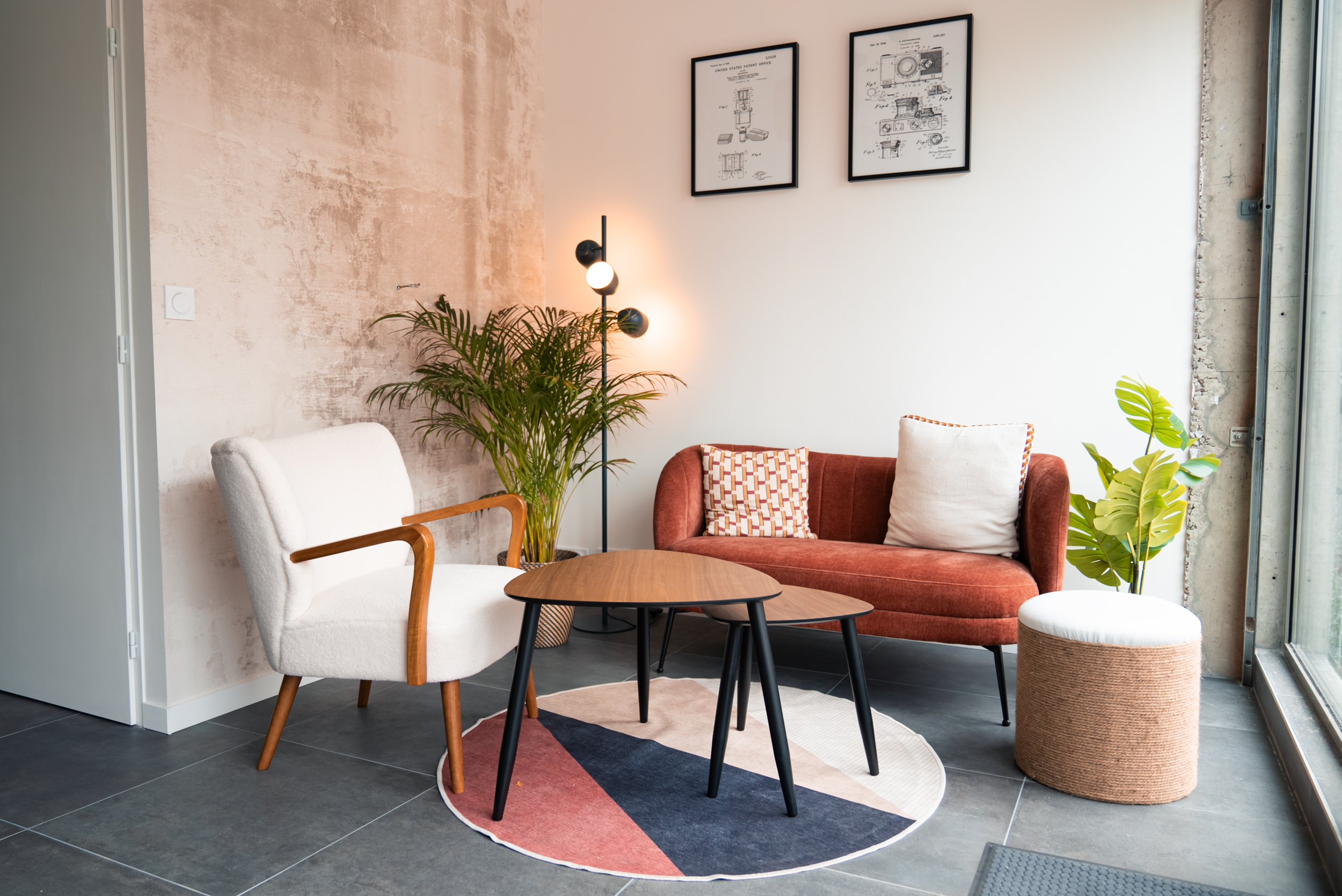 Séjour moderne avec canapé rouge, fauteuil blanc, tables basses, plantes, tapis coloré, lampes, tableaux.