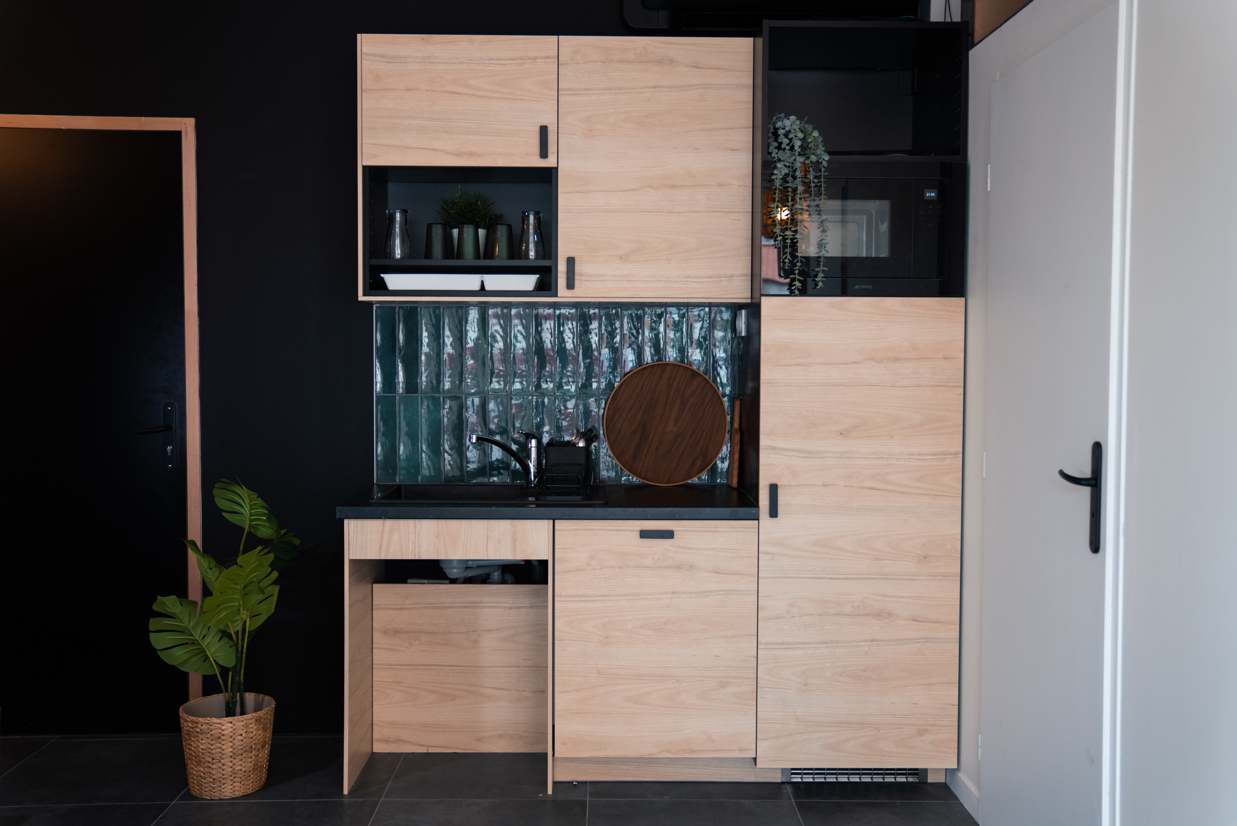 Cuisine moderne avec armoires en bois, plan de travail noir, évier et plantes.