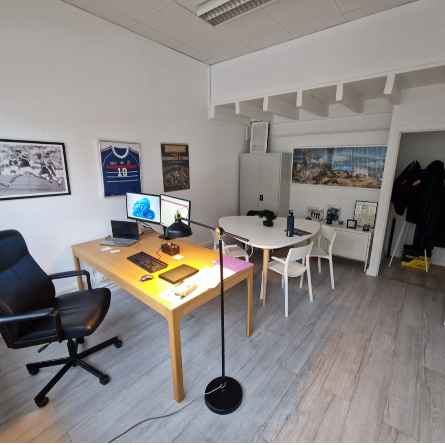 Bureau moderne avec chaise ergonomique, bureau en bois, ordinateurs, éclairage design, décoration murale, table ronde, chaises blanches, étagères, intérieur élégant.