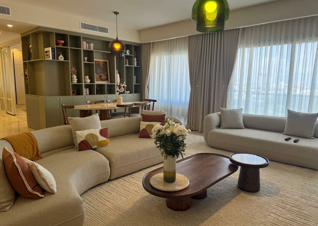 Séjour moderne avec canapés, table basse, fleurs, luminaires, bibliothèque, rideaux.