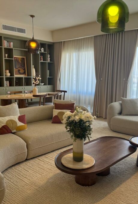 Séjour moderne avec canapés, table basse, fleurs, luminaires, bibliothèque, rideaux.