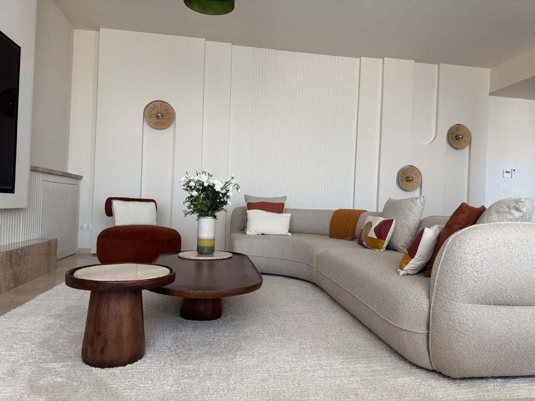 Salon moderne avec canapé, tables basses, fleurs, éclairage mural, décoration intérieure.