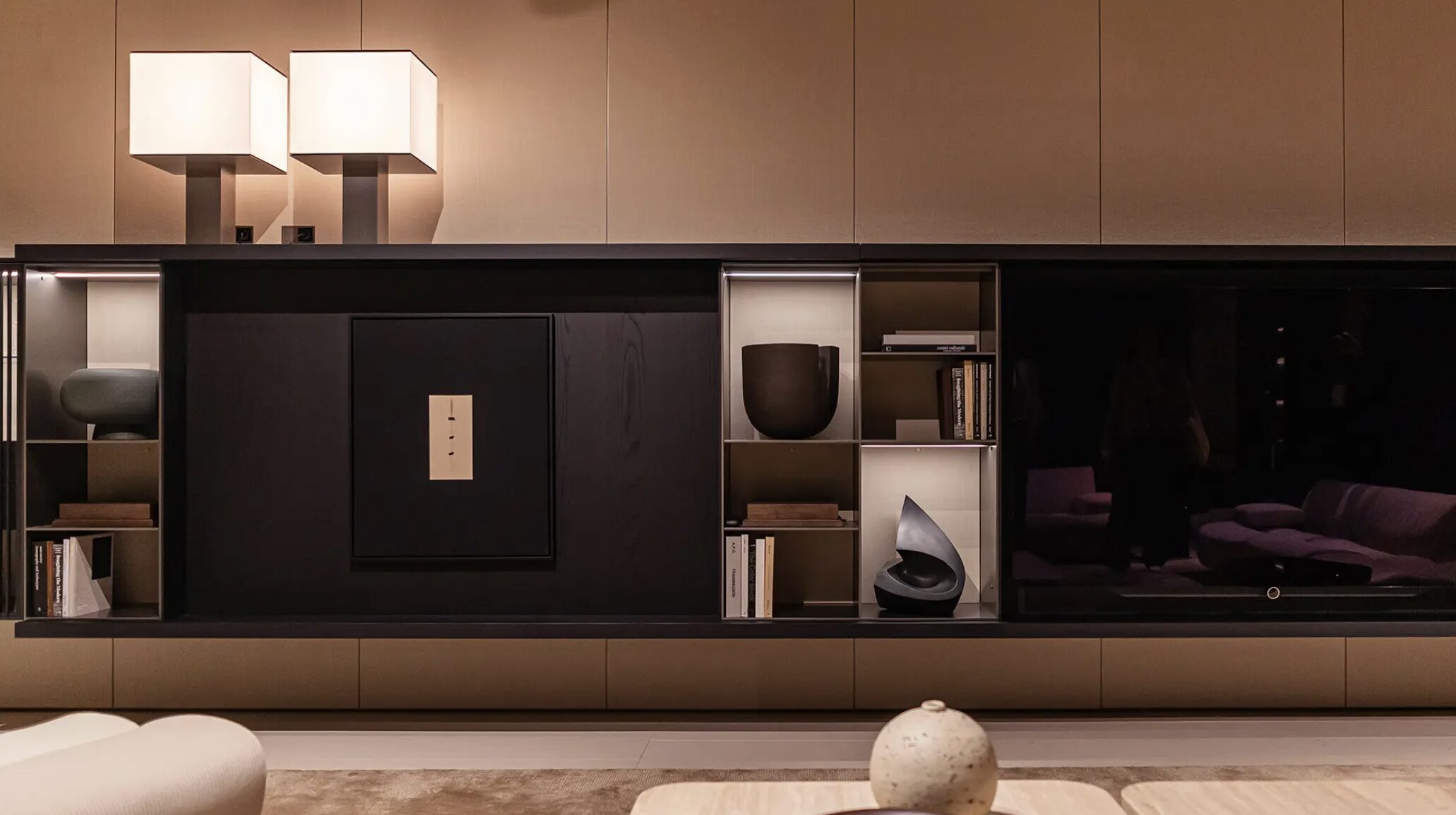 Modern living room with sleek TV unit, books, and lamps.