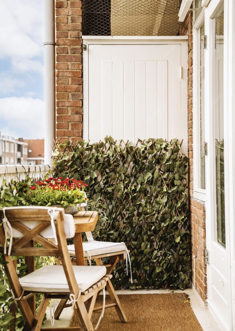 Petit balcon avec table et chaises en bois, plantes, écran vert, porte blanche
