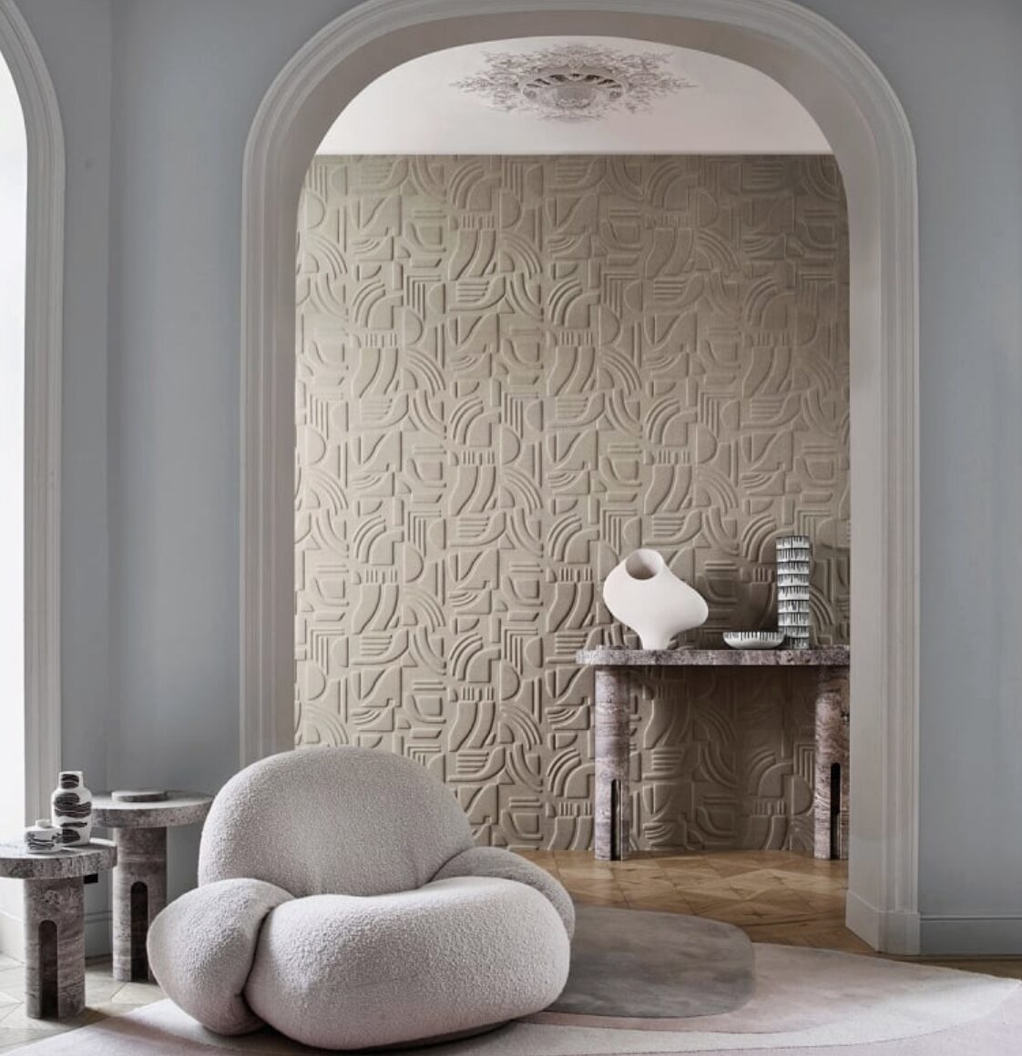 Intérieur moderne avec fauteuil moelleux, mur texturé, table basse, tapis, et cheminée.